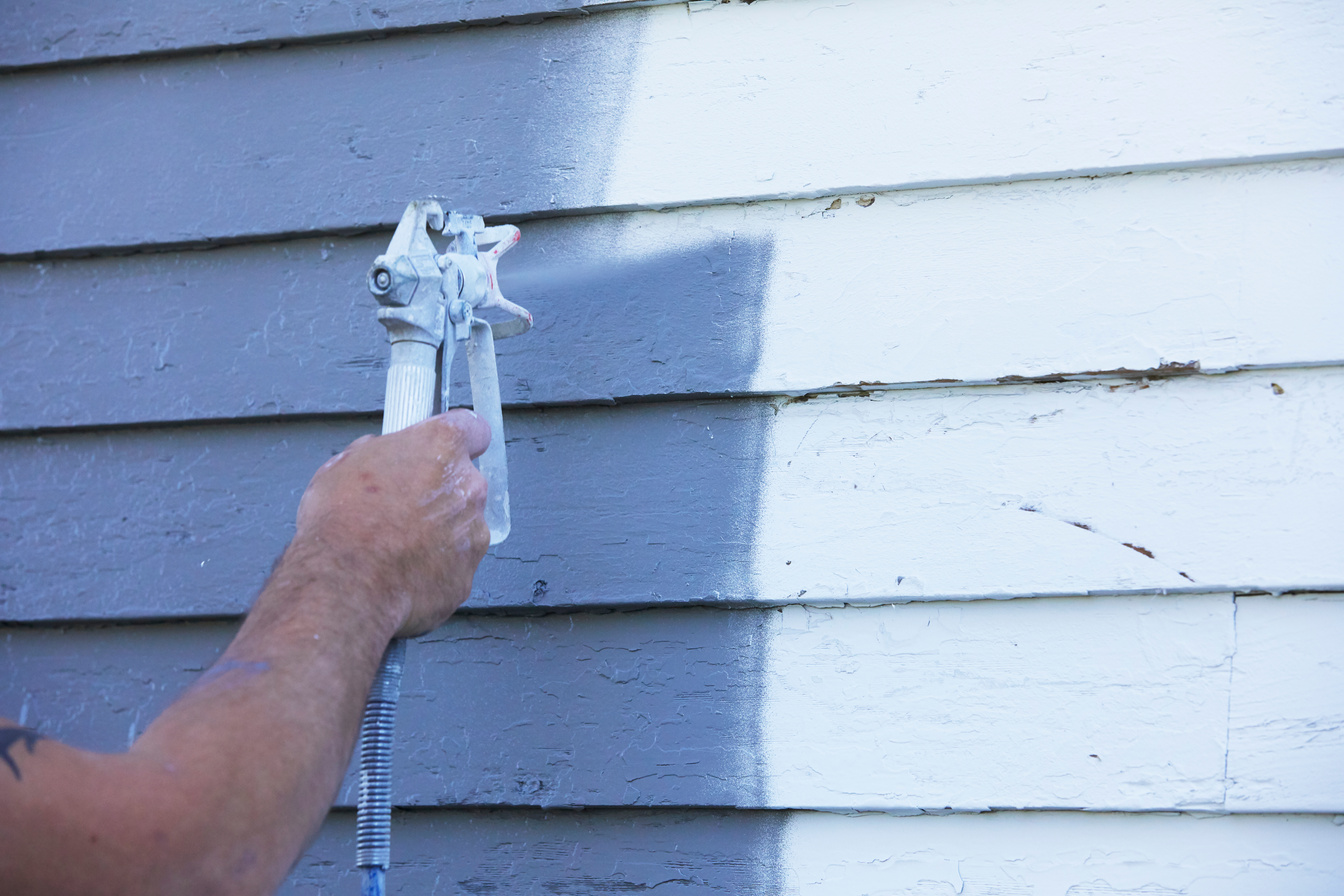 Man Spaying Paint On Exterior of Old Home